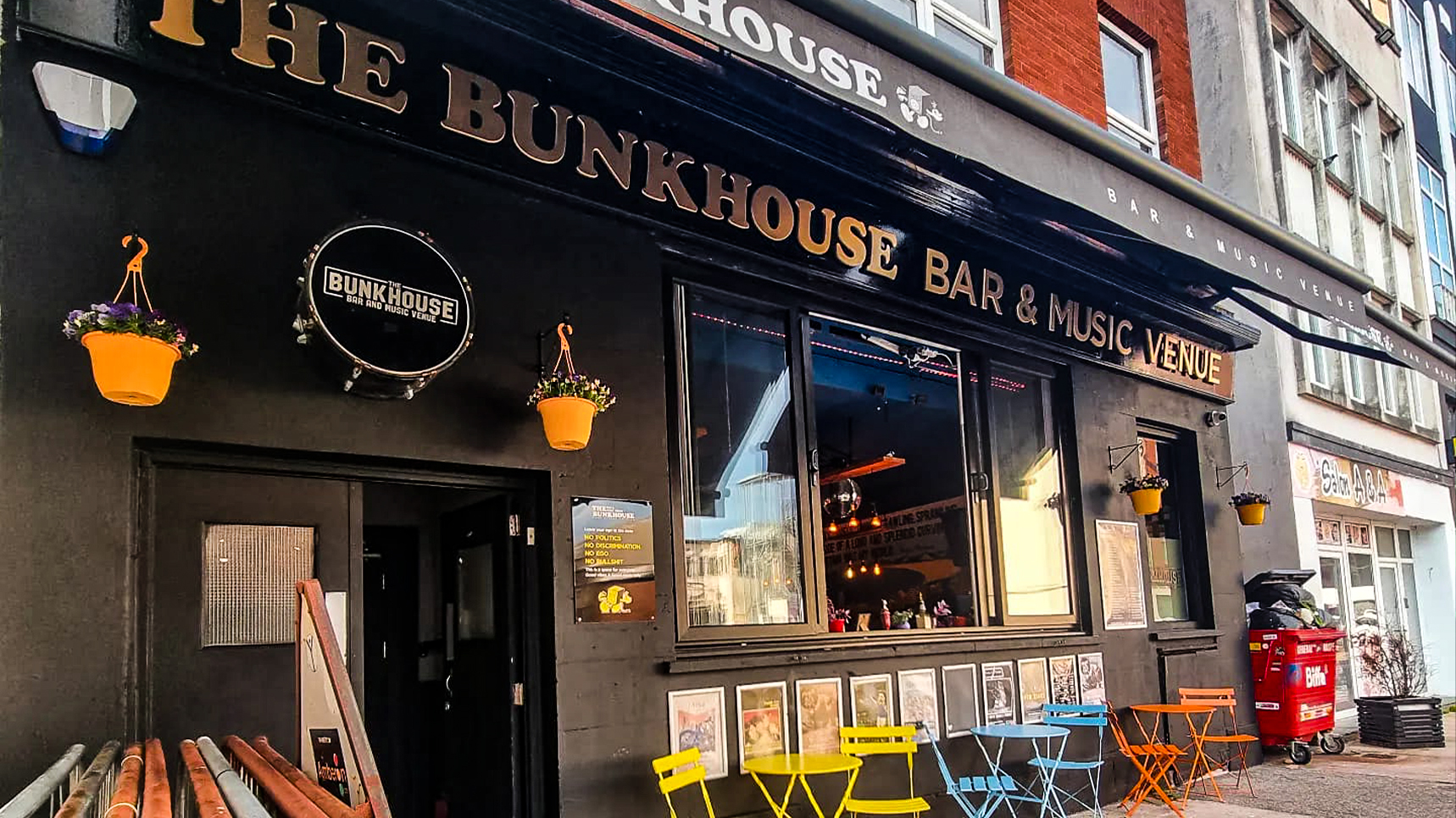 The dark painted exterior of The Bunkhouse bar and live music venue on Park Street in Swansea, featuring hanging flower baskets and outdoor seating.
