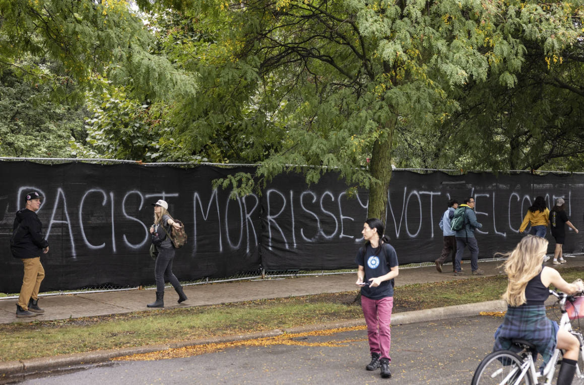Protest graffiti reading "RACIST MORRISSEY NOT WELCOME" along the Douglass Park perimeter fence at Riot Fest in Chicago.