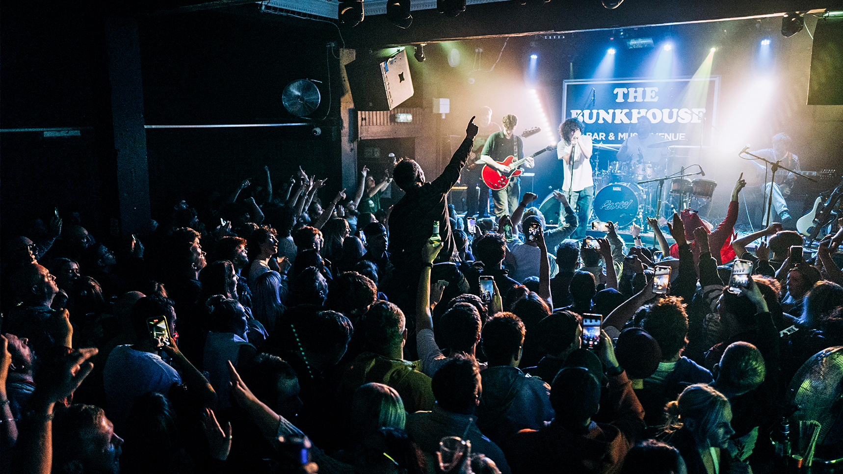 Live indie rock band Pastel performing on stage under bright lights to a packed, energetic crowd at The Bunkhouse Swansea.